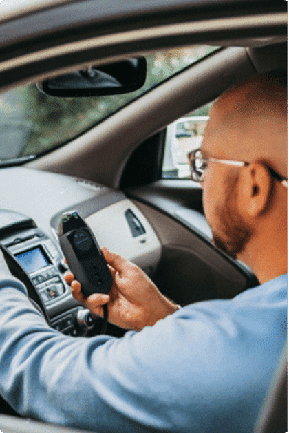 Man using a Smart Start ignition interlock breathalyzer device while sitting in his car