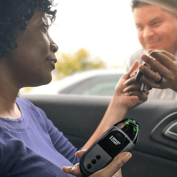 Woman holding a Smart Start 3030 ignition interlock device while a technician assists her